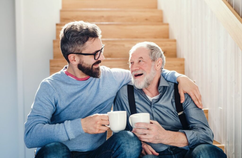 A loving son having a conversation with his senior father who has dementia while enjoying a cup of coffee by the stairs