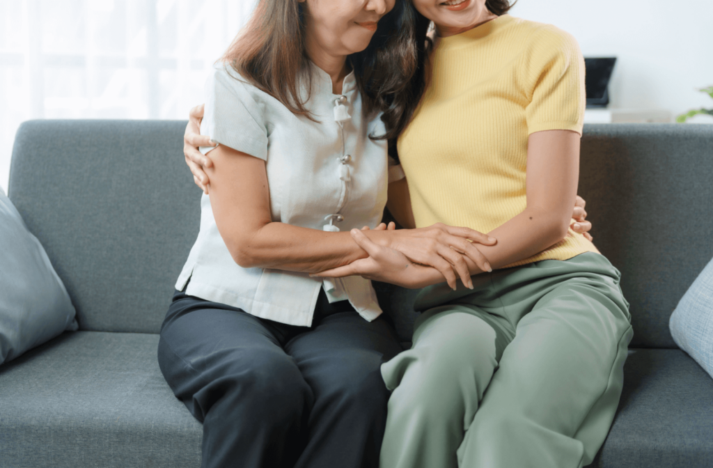 An adult child warmly embraces their senior parent on a couch.